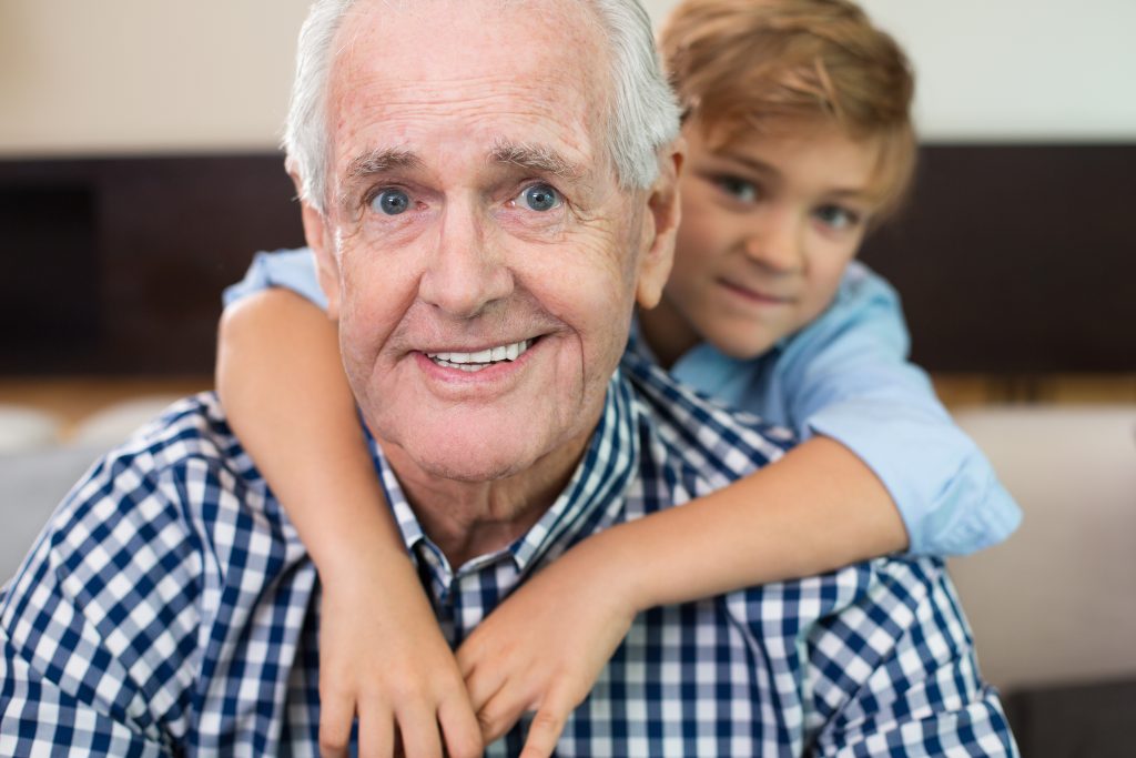 Portrait of little Caucasian grandson embracing happy grandfather, they looking at camera and smiling